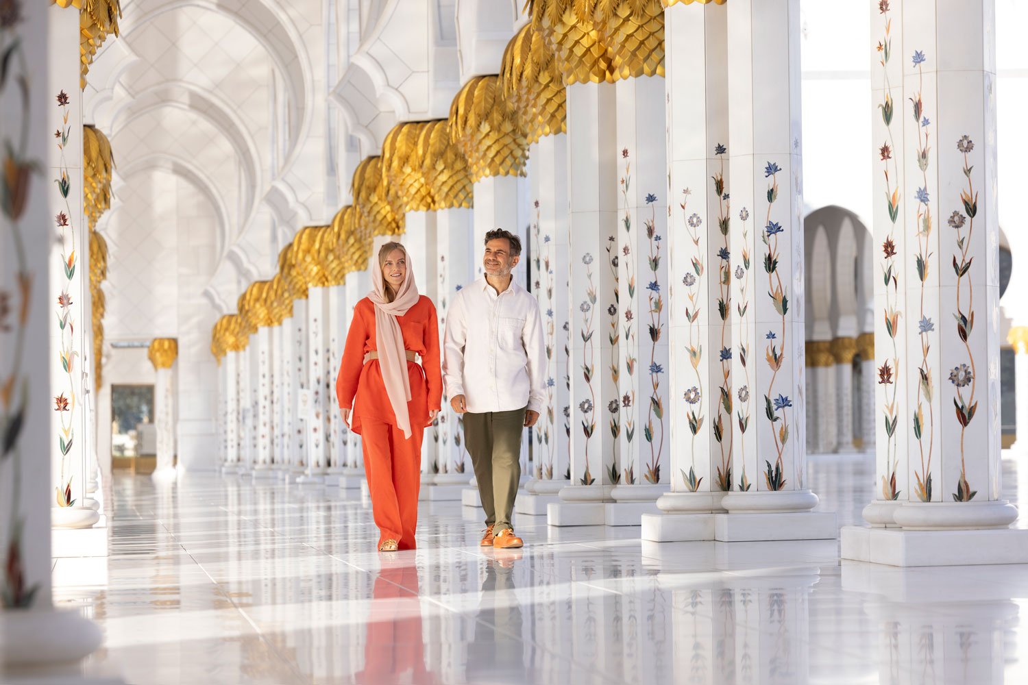 Couple walking through the elegant Sheikh Zayed Grand Mosque with stunning marble columns.