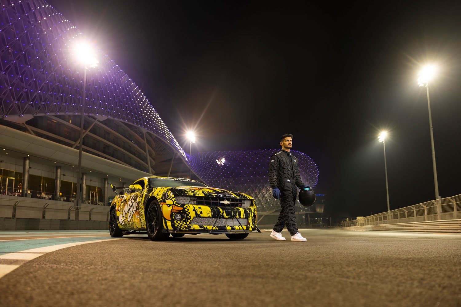 A racecar driver standing next to a custom-painted car at Yas Marina Circuit, Abu Dhabi